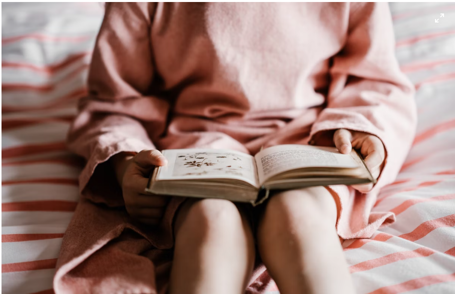 A child with ADHD sitting on a bed and reading a book about herbs